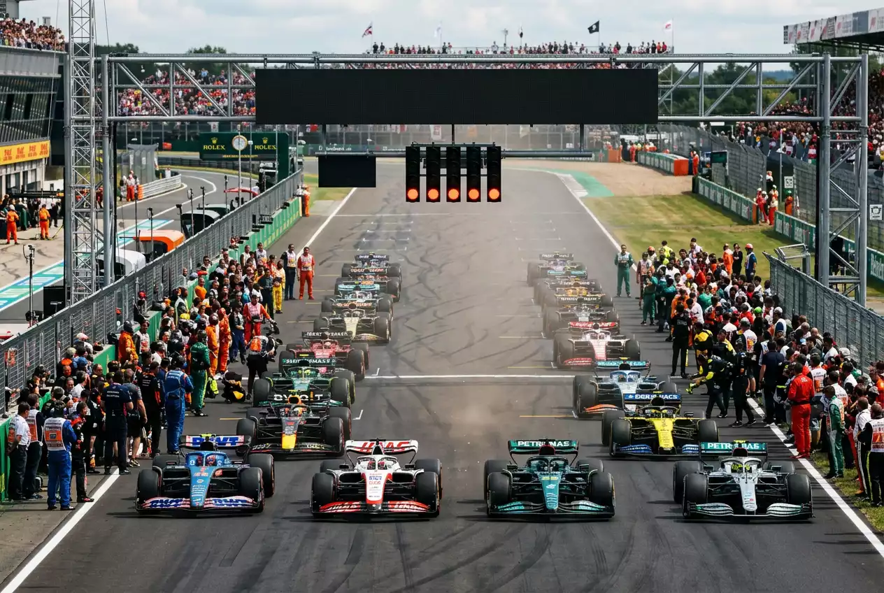 Row of Formula 1 cars lined up on a starting grid before the race with timing boards in the background